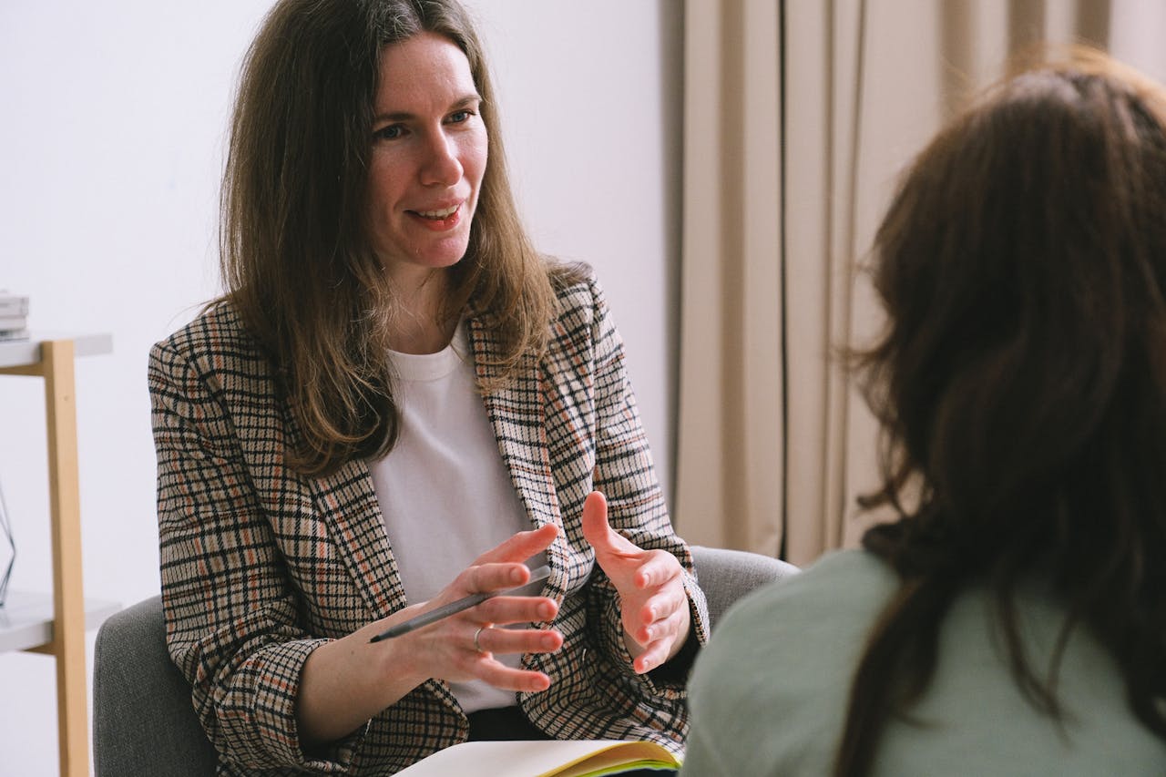 about-02 Pensive woman psychologist with brown hair in stylish clothes sitting and talking with unrecognizable female in light room