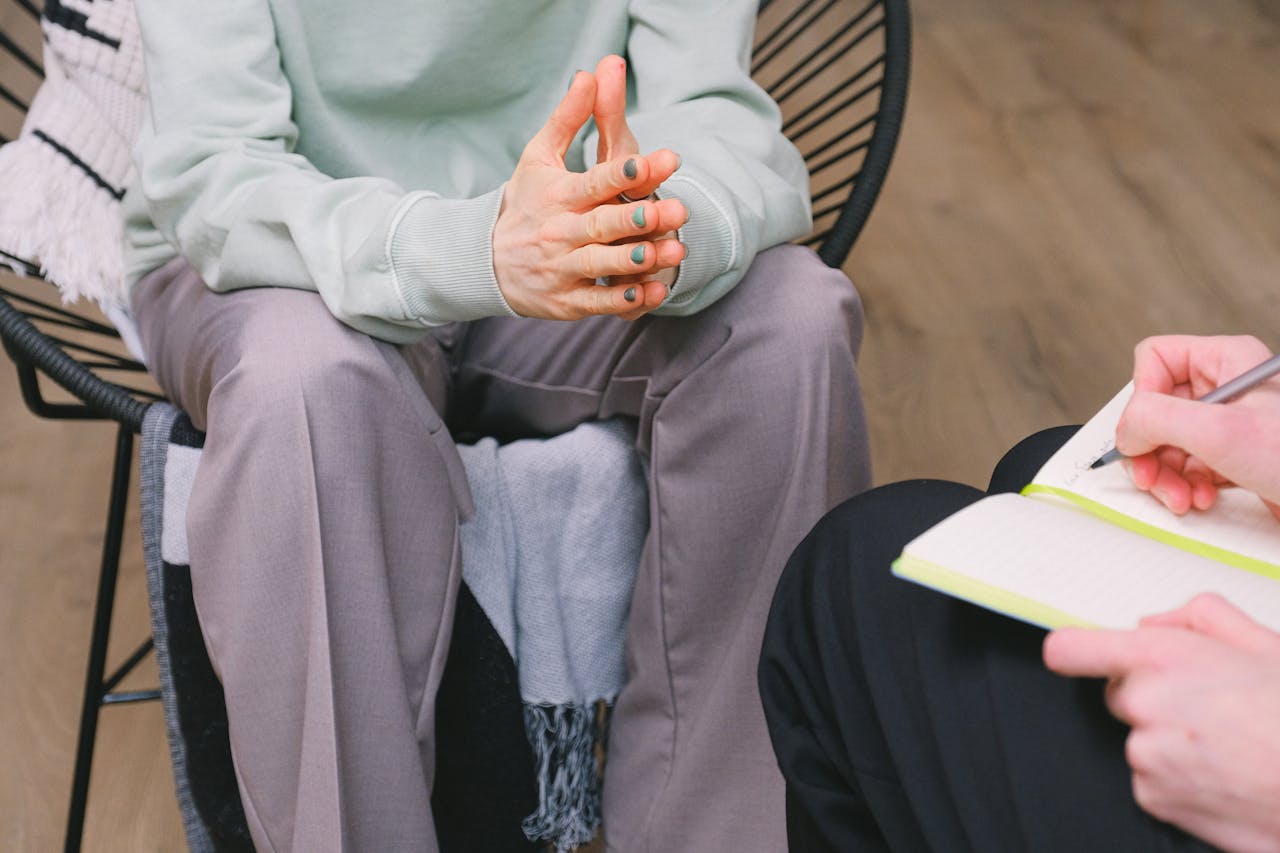 about-04 Crop unrecognizable psychotherapist taking notes in journal while interacting with woman on chair during psychological counseling indoors